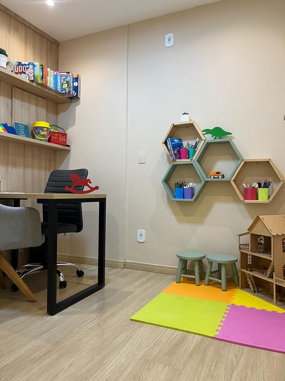 Sala de atendimento com tapete colorido, estantes de brinquedos e mesa